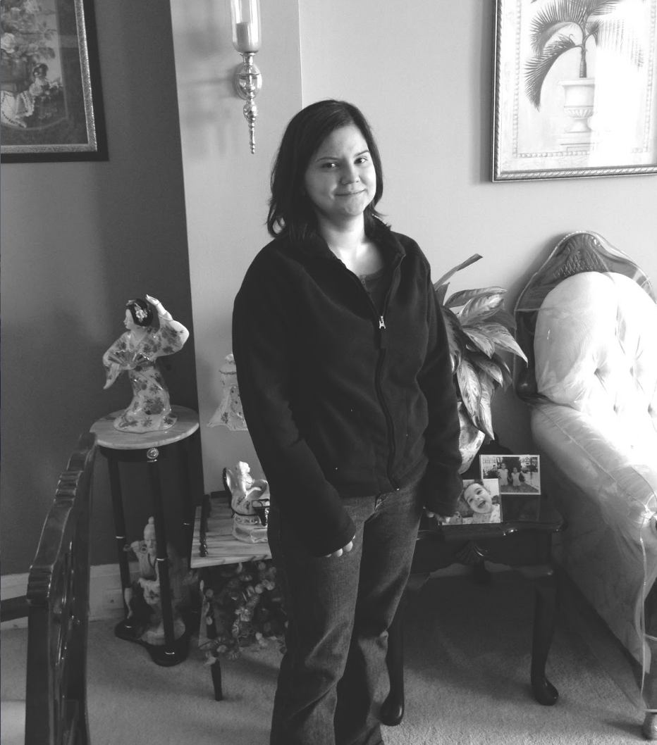 Black and white image of woman veteran standing in a living room in front of a series of side tables